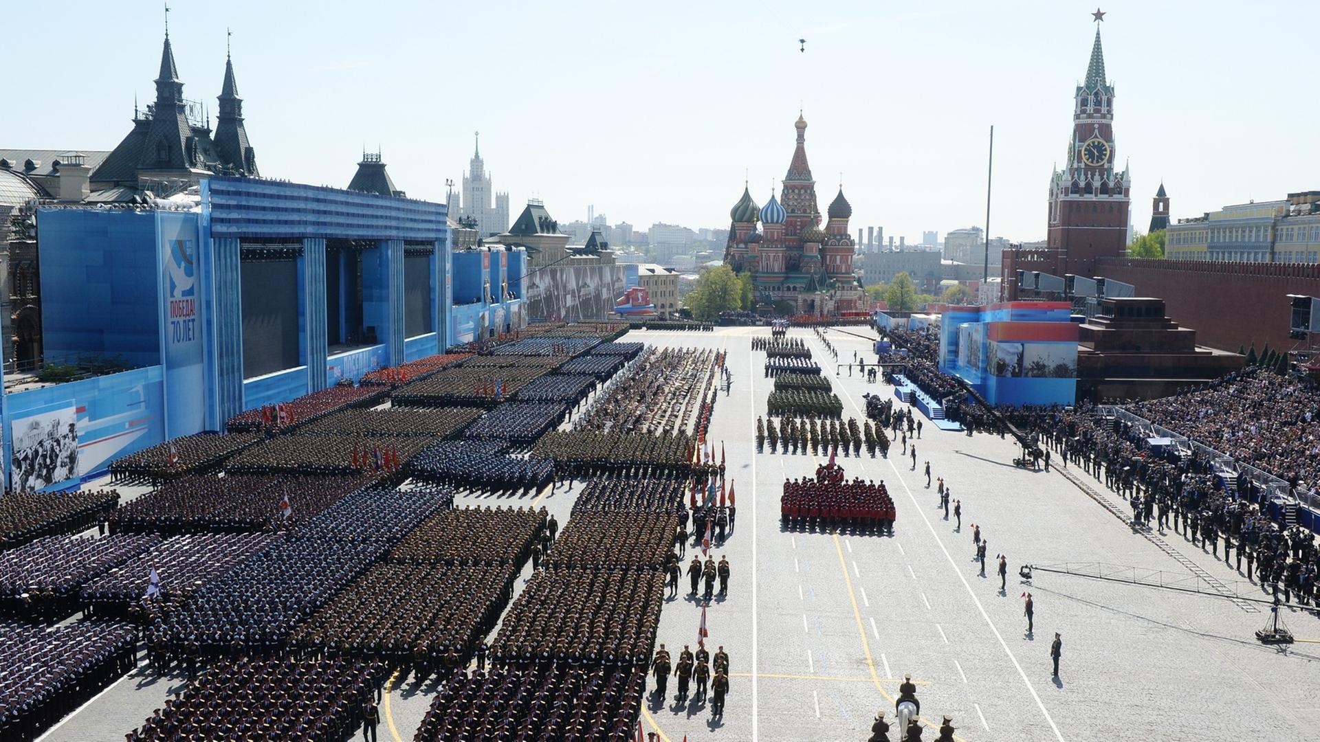 Militärparade in Moskau zum Gedenken an das Ende des Zweiten Weltkriegs, 9. Mai 2015, Blick von oben auf einen großen Platz, auf dem Soldatenformationen marschieren, im Hintergrund Skyline von Moskau.