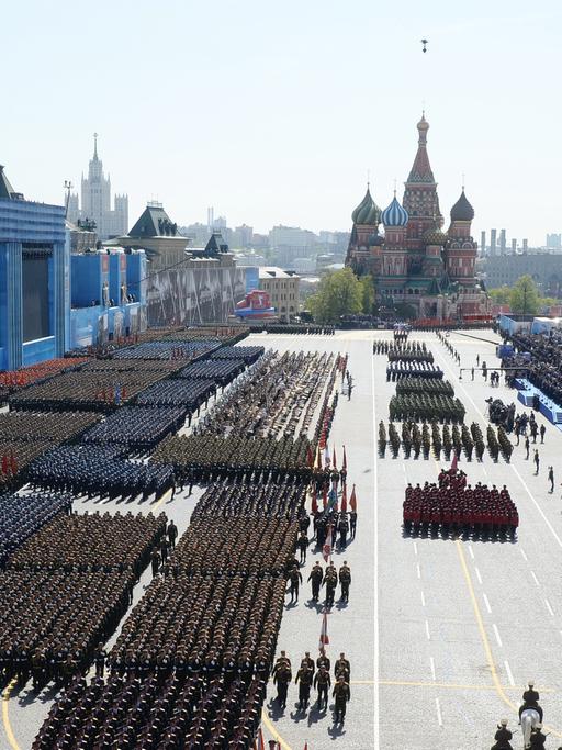 Militärparade in Moskau zum Gedenken an das Ende des Zweiten Weltkriegs, 9. Mai 2015, Blick von oben auf einen großen Platz, auf dem Soldatenformationen marschieren, im Hintergrund Skyline von Moskau.