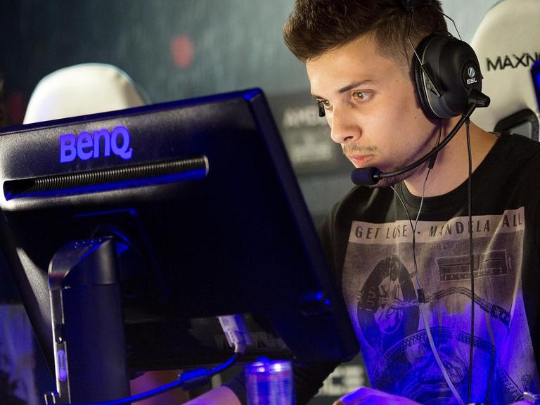 Ein Spieler sitzt mit Kopfhörer und Mikrofon vor einem Monitor.