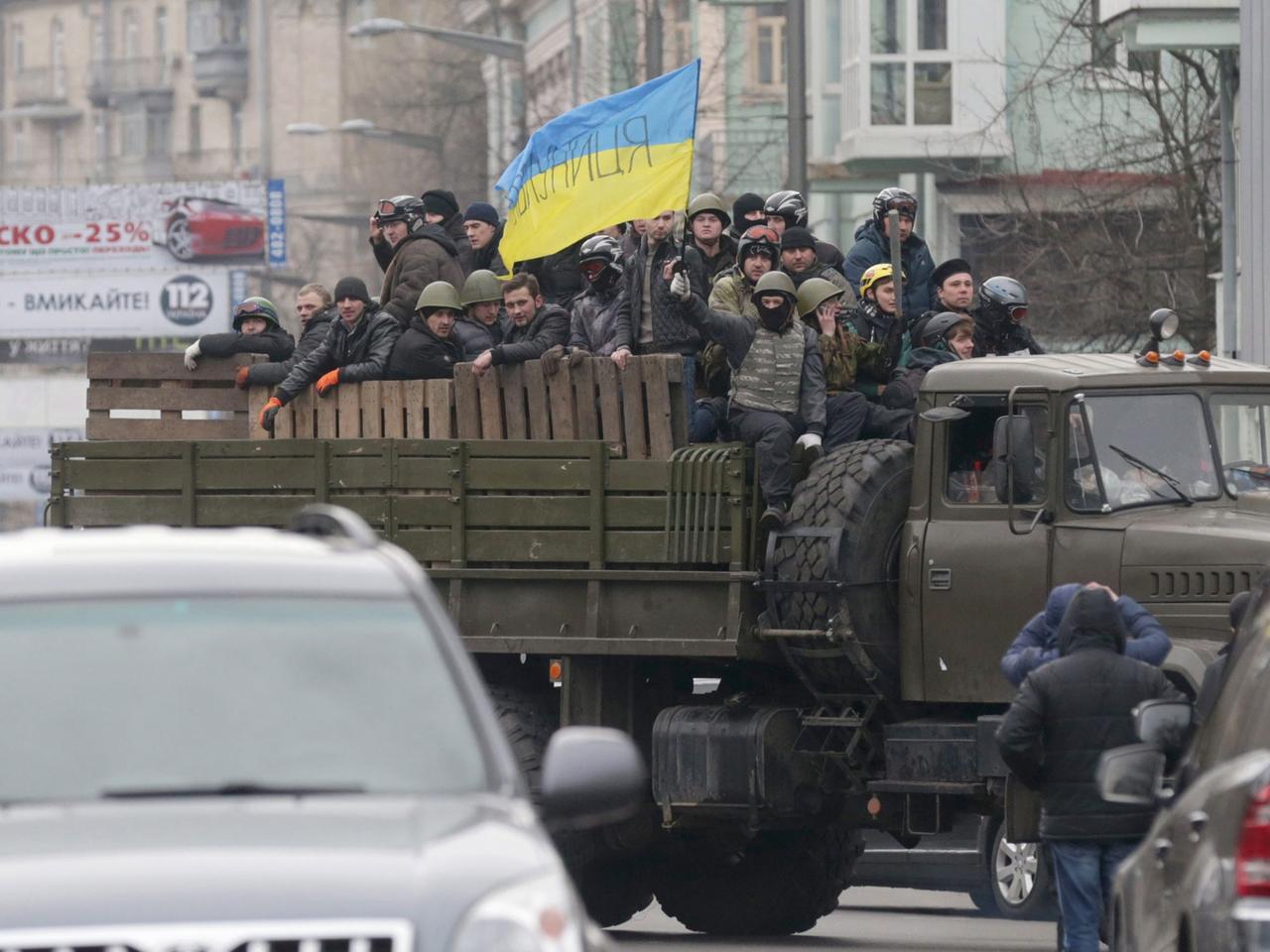 Vermummte Demonstranten auf einem Lastwagen schwenken eine ukrainische Flagge.