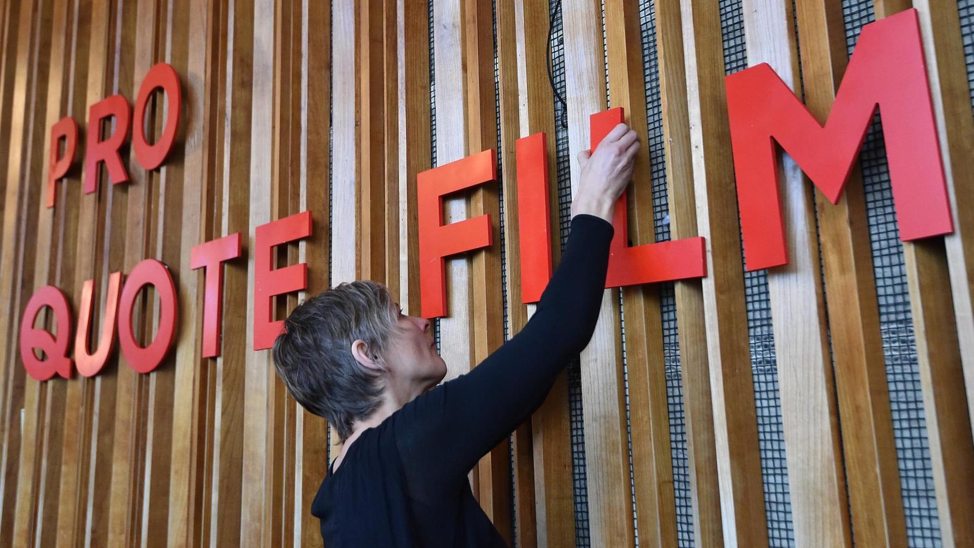 31.01.2018, Berlin: Ein Frau bringt im Kino Kosmos den Slogan "Pro Quote Film" an. Der neue Zusammenschluss von Frauen aus allen Gewerken der Filmbranche erweitert die bisherige Arbeit des Zusammenschlusses von Regisseurinnen auf die Gleichstellung von Frauen in allen Bereichen des Films. Foto: Bernd Settnik/dpa-Zentralbild/dpa | Verwendung weltweit