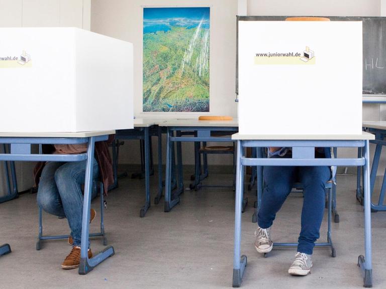 Schüler sitzen in einem Klassenzimmer hinter selbstgebauten Wahlkabinen mit der Aufschrift "Juniorwahl"