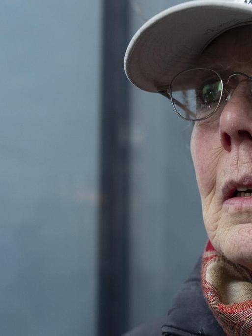 Die Schriftstellerin trägt ein Basecap und eine Brille und steht vor einer Glasfassade Die Schriftstellerin trägt ein Basecap und eine Brille und steht vor einer Glasfassade