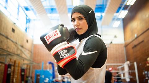 Zeina Nassar, Boxerin, steht in der TSC-Boxhalle und hält die Boxhandschuhe hoch.