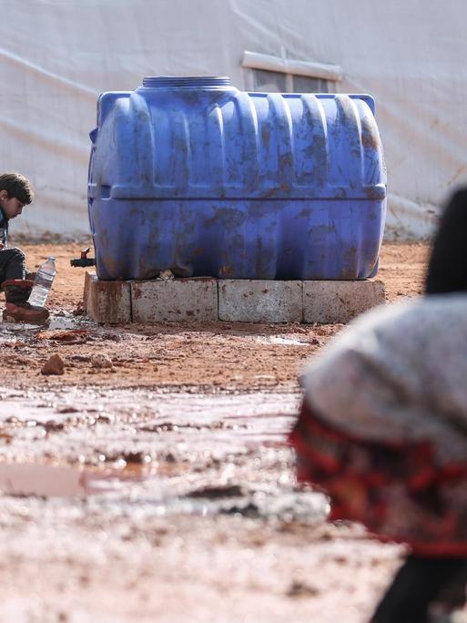 Syrische Kinder füllen in einem provisorischen Lager für Familien, die infolge der Bombardierung und der Militäroperationen aus dem Idlib-Land vertrieben wurden, Krüge mit Wasser auf.