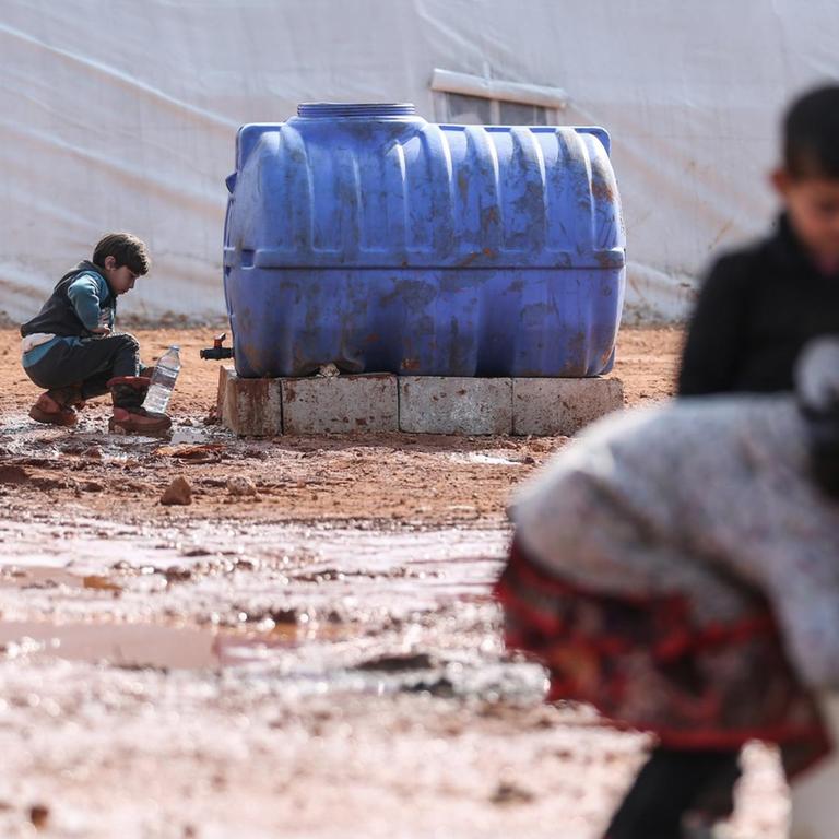 Syrische Kinder füllen in einem provisorischen Lager für Familien, die infolge der Bombardierung und der Militäroperationen aus dem Idlib-Land vertrieben wurden, Krüge mit Wasser auf.