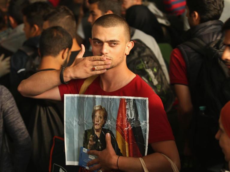 Ein vermutlich aus Syrien stammender Flüchtling macht eine Kusshand und hält dabei ein Bild von Angela Merkel in die Kamera, während er und etwa 800 weitere Personen aus Ungarn am 5. September 2015 am Münchner Hauptbahnhof in München eintreffen.