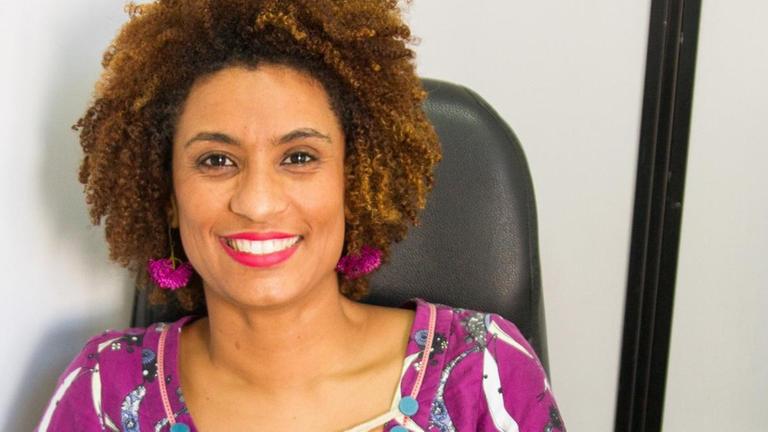 Ein Porträt der brasilianischen Politikerin Marielle Franco. Sie trägt einen Afro und lächelt offen in die Kamera.