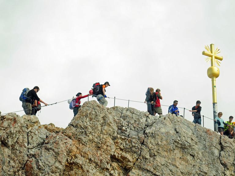 Mehrere Bergsportler klettern bei Garmisch-Partenkichen (Oberbayern) auf der Zugspitze in Richtung Gipfelkreuz.