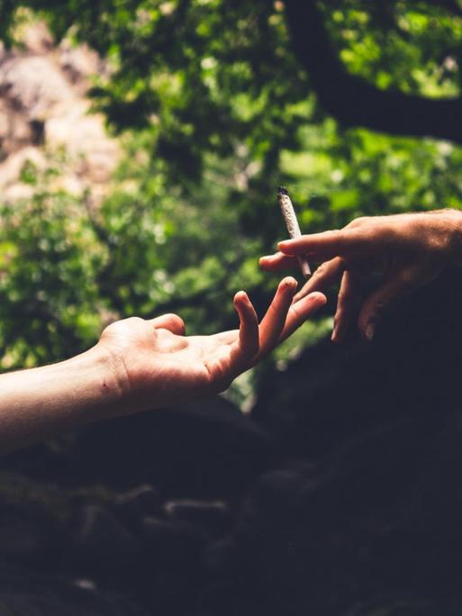 Zwei Hände reichen sich einander, in der einen wir eine Zigarette gehalten.