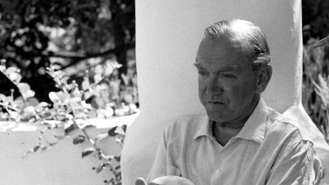 Graham Greene sitzt auf einer Terrasse im Garten.