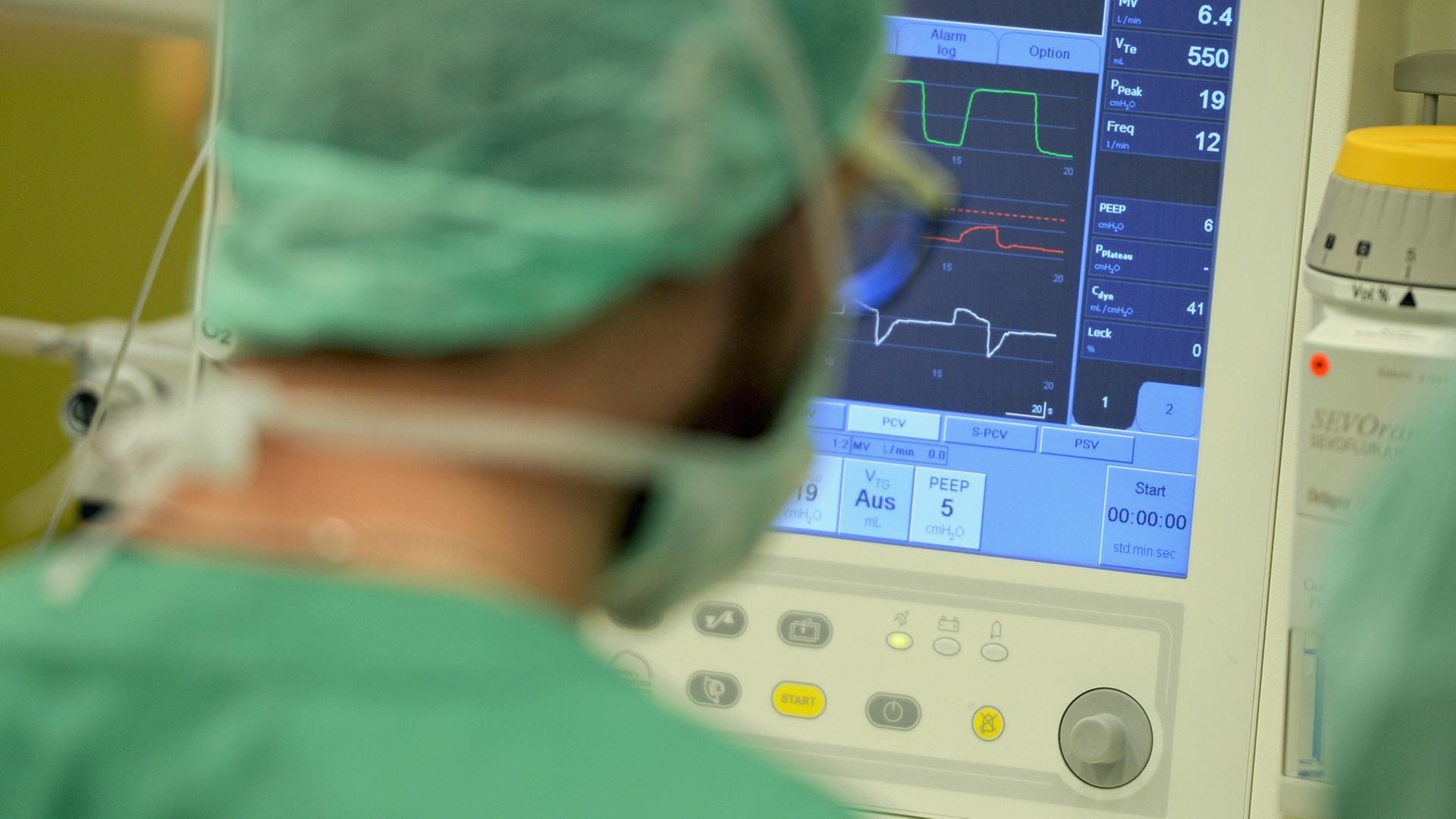 Ein Mediziner schaut in einer Klinik während einer Operation auf einen Überwachungs-Monitor.