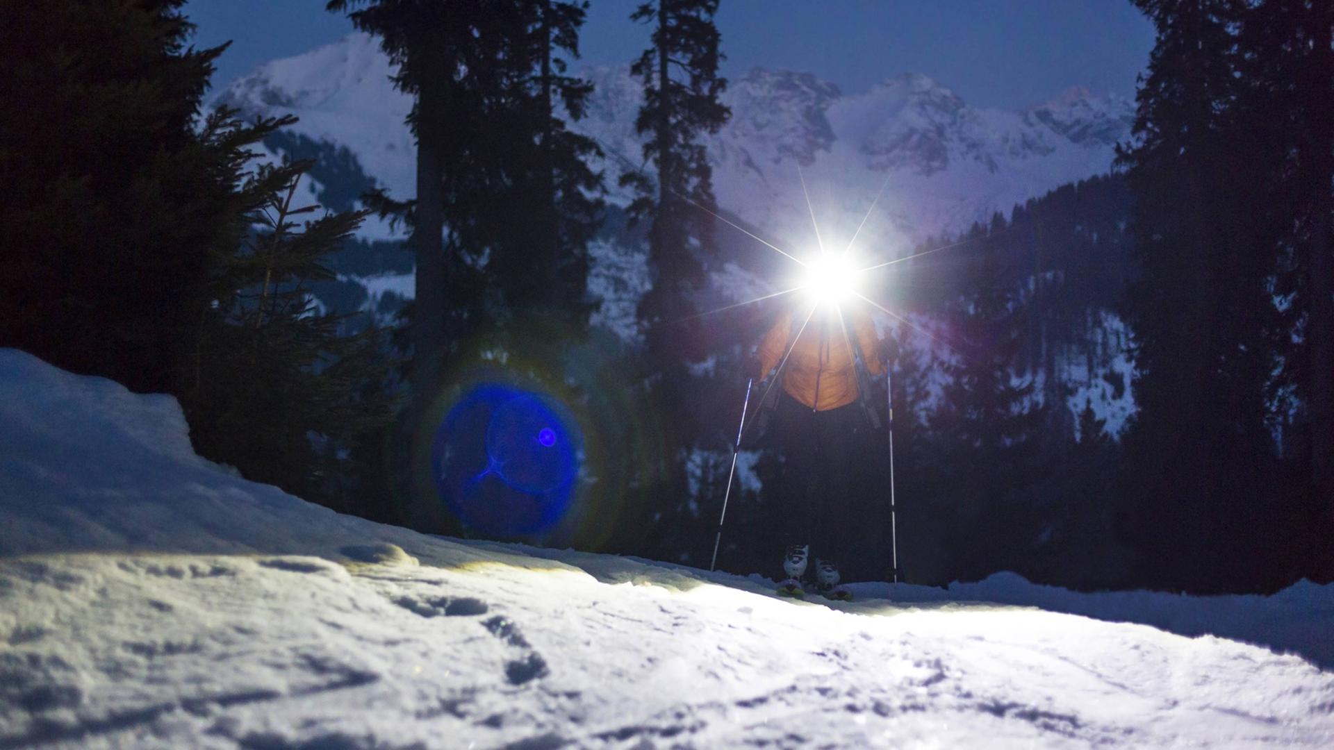 Ein Skilangläufer mit einer Stirnlampe läuft bei Nacht einen Berg hoch.