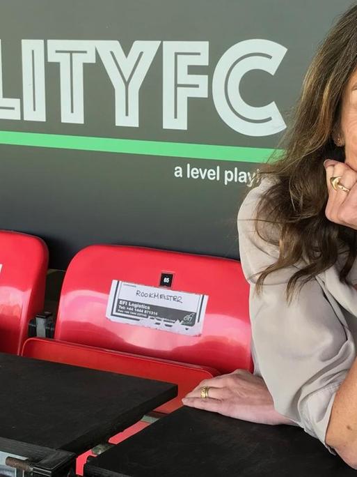 Karen Dobres sitzt im Stadion vor einem Plakat mit der Aufschrift "Equality FC".