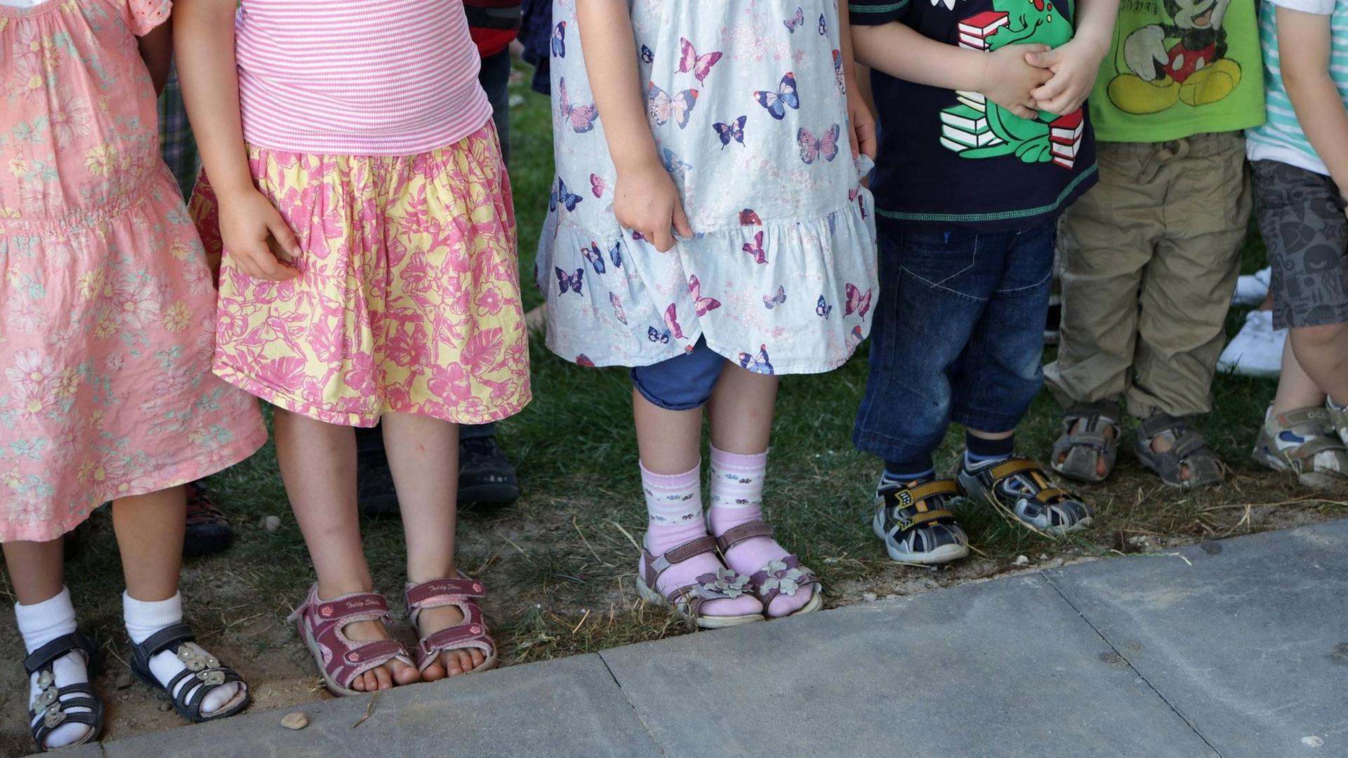Symbolbild Kindertagesstätte: Füße und Beine von Kindern, die in einer Reihe stehen.