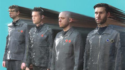 Vier graugekleidete Männer stehen vor einer blauen Wand.