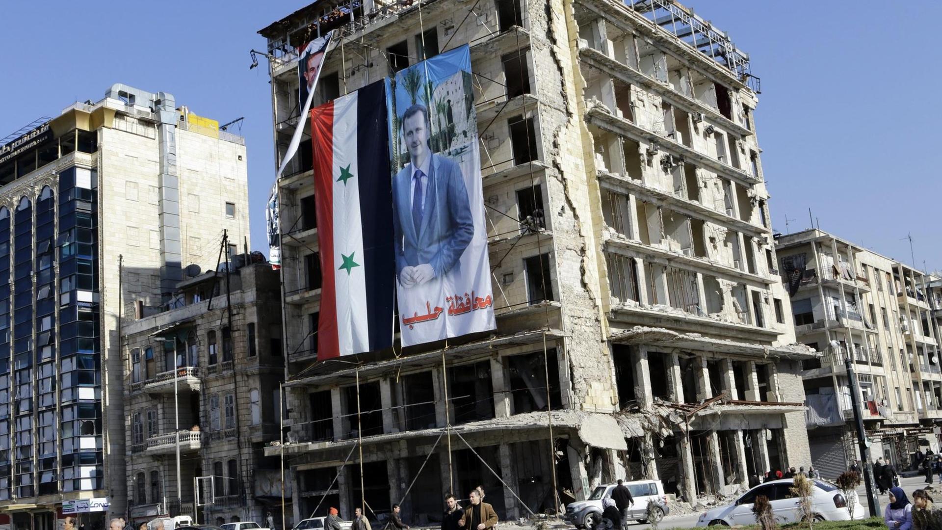 Ein Banner mit dem syrischen Machthaber Baschar al-Assad hängt in Aleppo von einem zerstörten Gebäude.