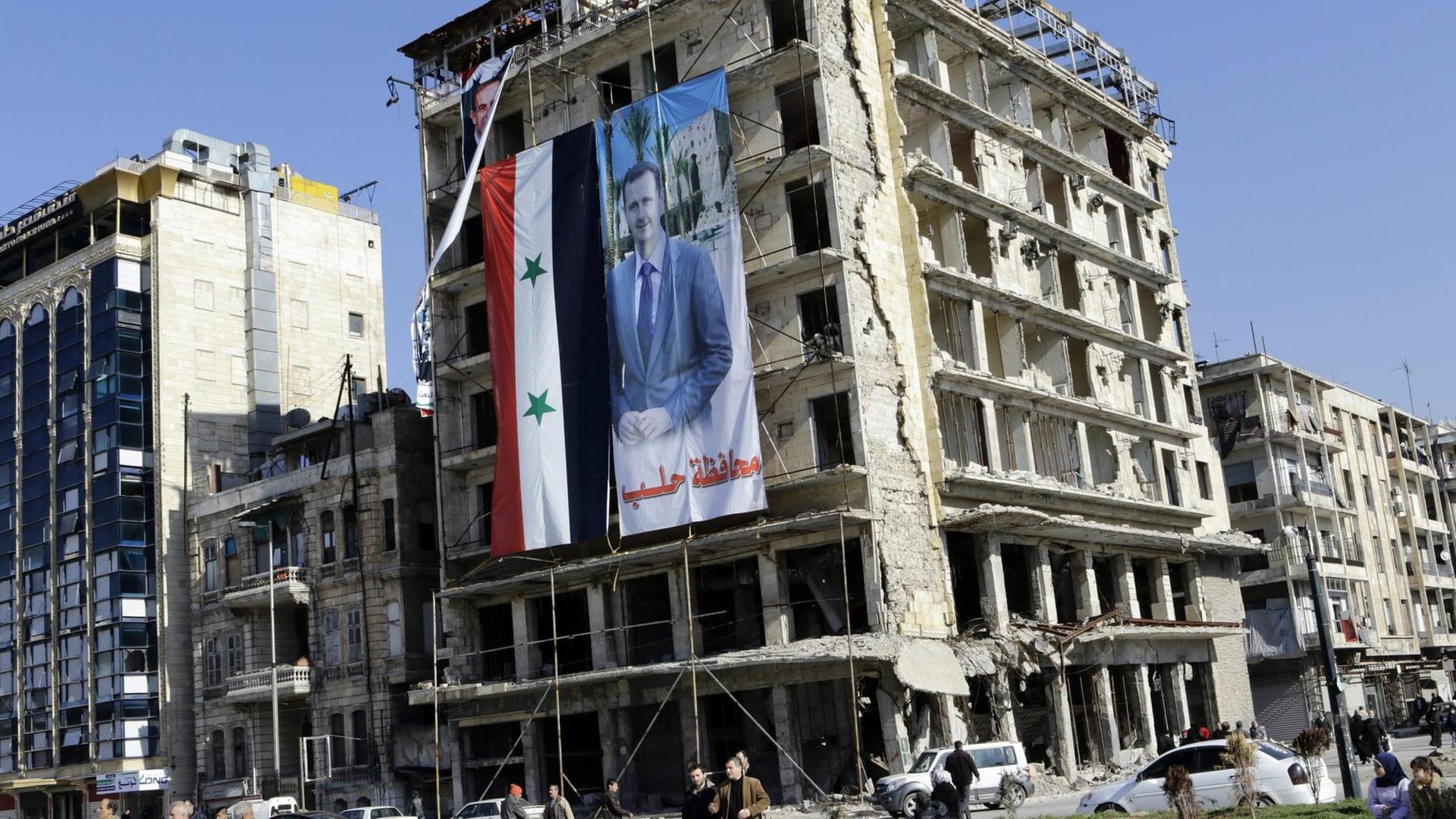 Ein Banner mit dem syrischen Machthaber Baschar al-Assad hängt in Aleppo von einem zerstörten Gebäude. Ein Banner mit dem syrischen Machthaber Baschar al-Assad hängt in Aleppo von einem zerstörten Gebäude.
