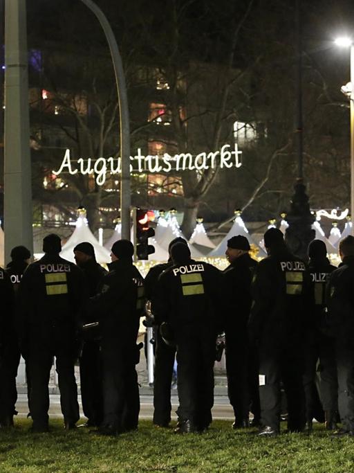 Polizisten stehen am 21.12.2015 in Dresden (Sachsen) am Rande einer Kundgebung des Bündnisses Pegida (Patriotische Europäer gegen die Islamisierung des Abendlandes) an einer Straße, während im Hintergrund der sogenannte Augustusmarkt zu sehen ist.
