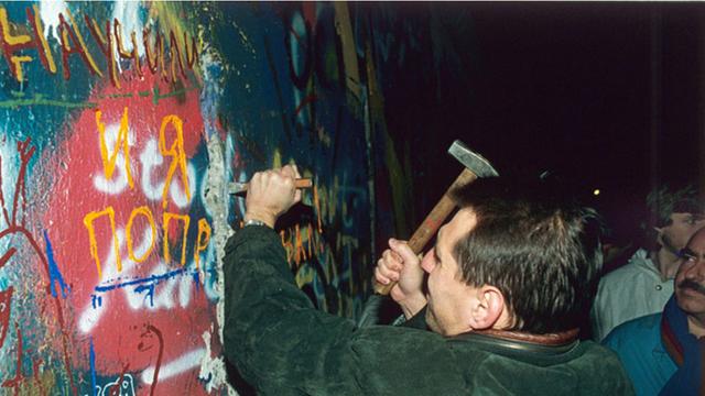 Ein Mann hämmert am 12.11.1989 ein Loch in die mit Graffitis bemalte Berliner Mauer.