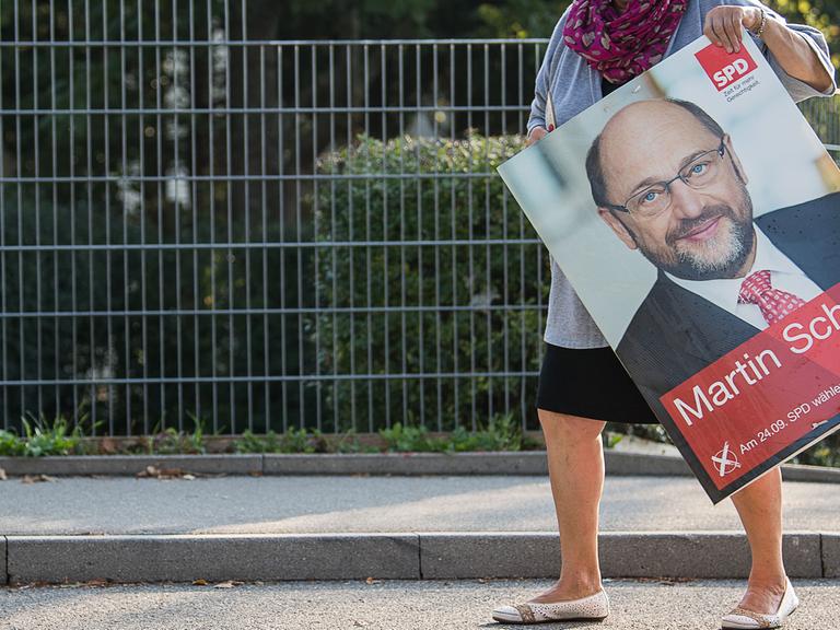 Eine Frau trägt am am 25.09.2017 in Stuttgart (Baden-Württemberg) nach der Bundestagswahl ein abgehängtes SPD-Wahlplakat mit Spitzenkandidat Schulz zu ihrem Auto.