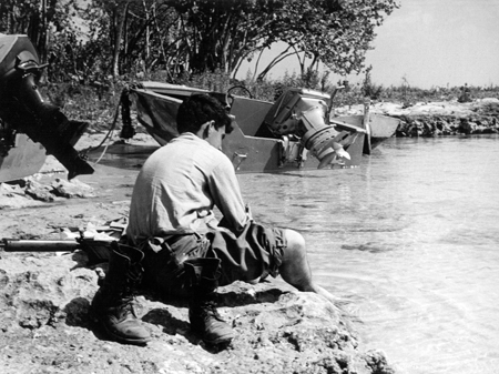 Neben zerstörten Landungsbooten der Invasionstruppen kühlt sich ein siegreicher Castro-Soldat in der Schweinebucht 1961 die Füße im Wasser.