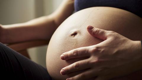 Eine schwangere Frau legt ihre Hand auf den Bauch (Symbolfoto).
