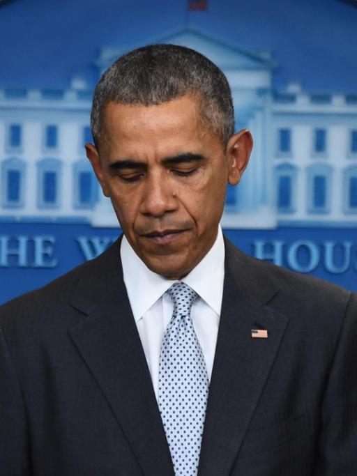 Obama steht vor dem Signum des Weißen Hauses und einer US-Flagge und schaut zu Boden.