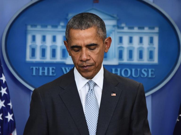 Obama steht vor dem Signum des Weißen Hauses und einer US-Flagge und schaut zu Boden.
