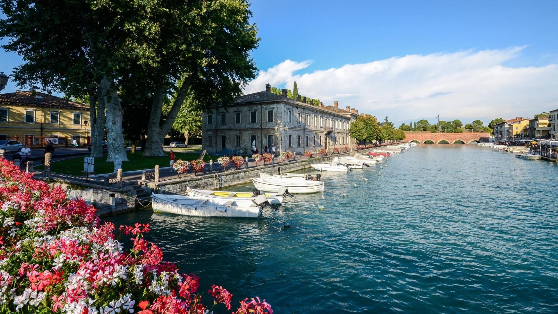 Blumen und kleine Boote am Ufer der Stadt Peschiera am Gardasee