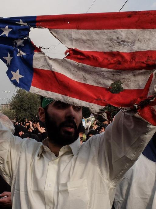 Während einer Anti-USA-Demonstration im Iran hält ein Teilnehmer eine zerrissene US-Flagge hoch.