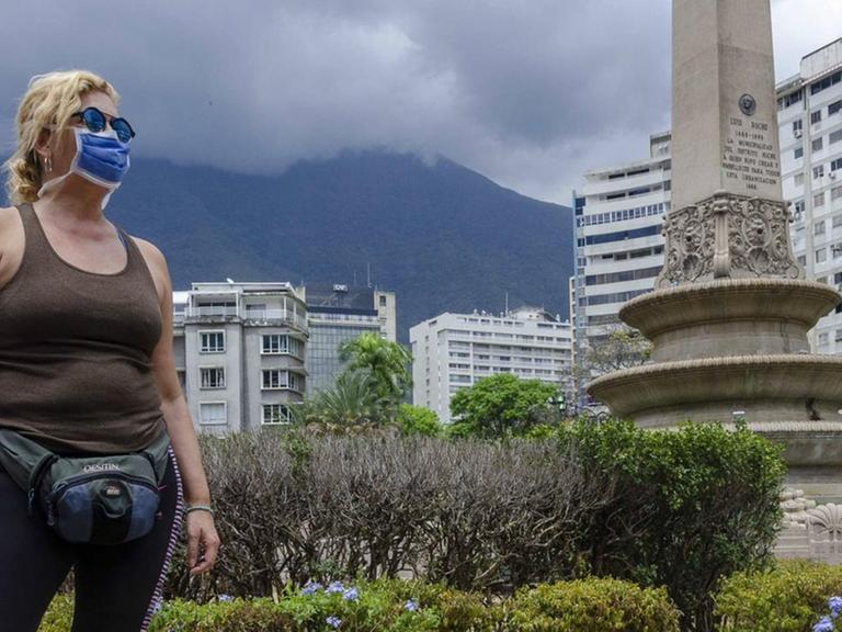 Eine Frau mit Schutzmaske steht trotzig auf einem Platz in Caracas.