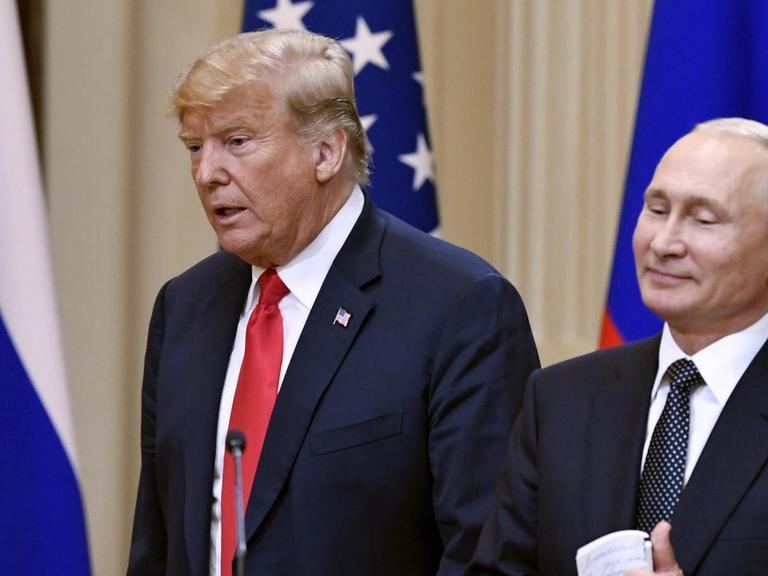 Trump sagt etwas, Putin steht lächelnd daneben. Vor ihnen ein Schild mit der Aufschrift "Helsinki 2018", hinter ihnen die Fahnen beider Staaten.