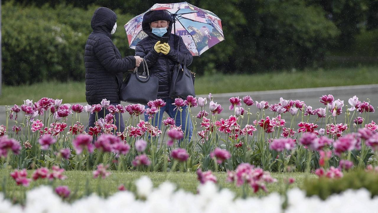 Zwei Personen mit Schutzmaske stehen in einem Park in Moskau und unterhalten sich.