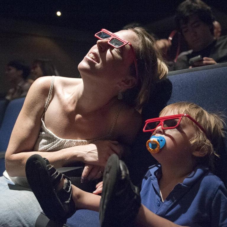 Eine Mutter mit Kleinkind schauen einen Film im 3D-Kino an.