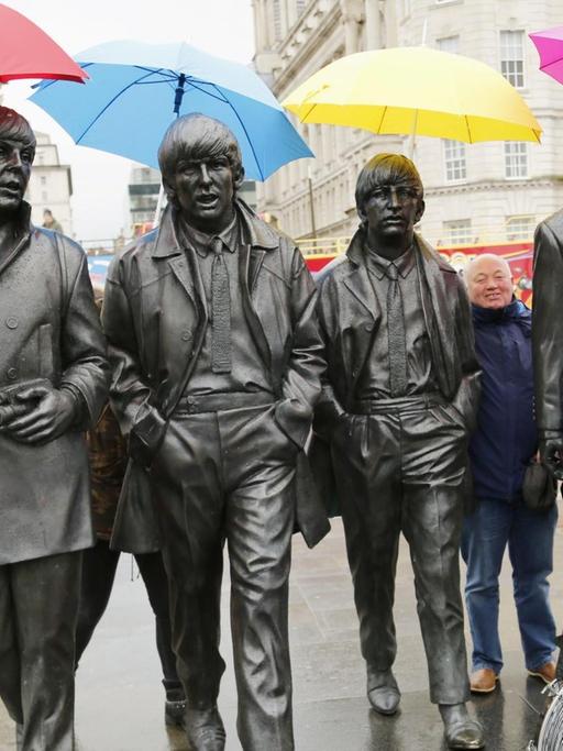 Liverpool feiert den 50. Geburtstag des Beatles Albums "Sgt. Pepper's Lonely Hearts Club Band". Menschen halten bunte Regenschirme über die Köpfe eines Denkmals zuehren der Gruppe.