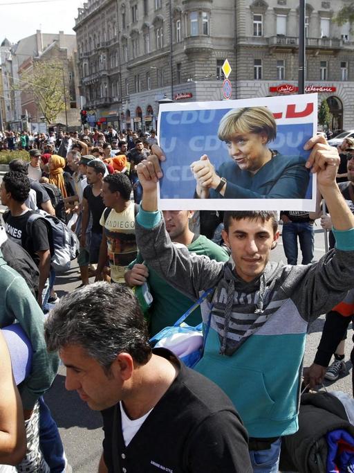 Hunderte Flüchtlinge laufen auf einer Straße. Ein Mann hält ein Plakat von Bundeskanzlerin Angela Merkel in die Höhe.