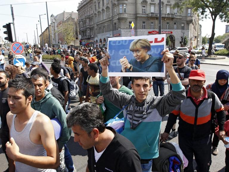 Hunderte Flüchtlinge laufen auf einer Straße. Ein Mann hält ein Plakat von Bundeskanzlerin Angela Merkel in die Höhe.
