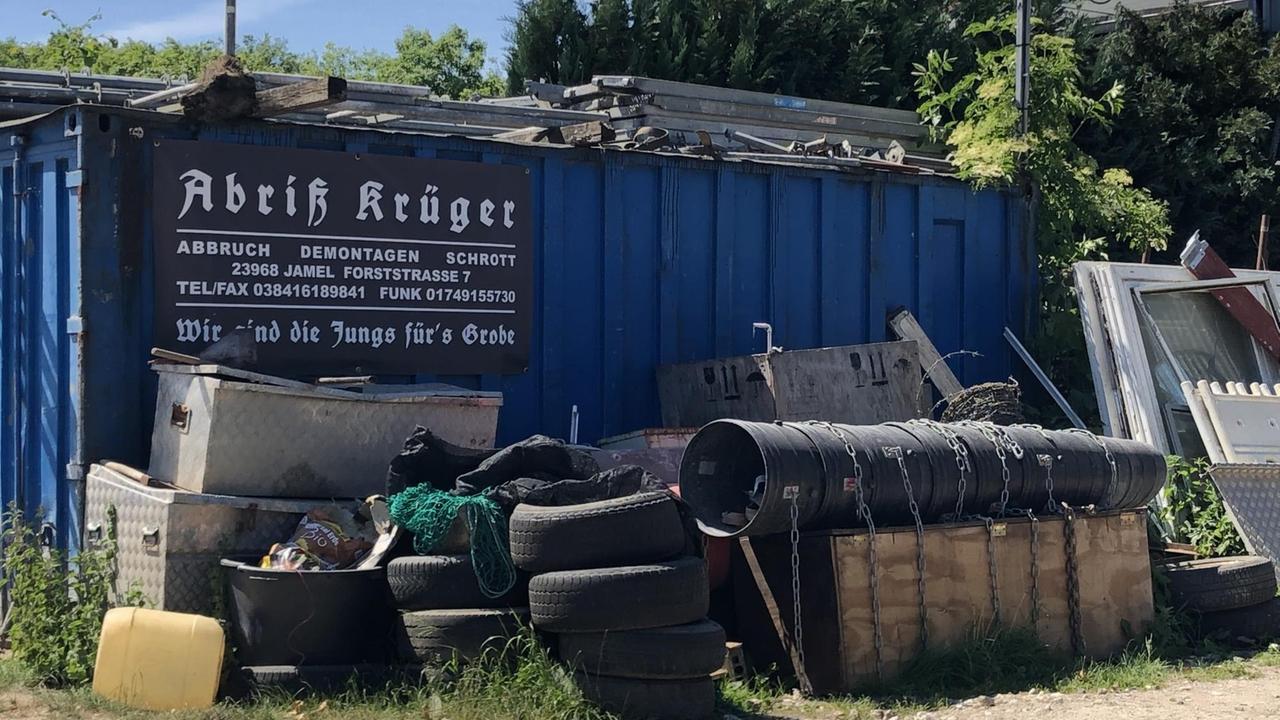 An einem Container ist das Schild "Abriß Krüger" angebracht, davor steht Sperrmüll und Gerümpel.