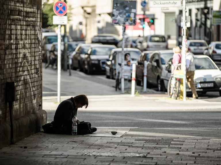 Ein Mann sitzt in einer Unterführung vor einem Schälchen auf dem Gehweg.