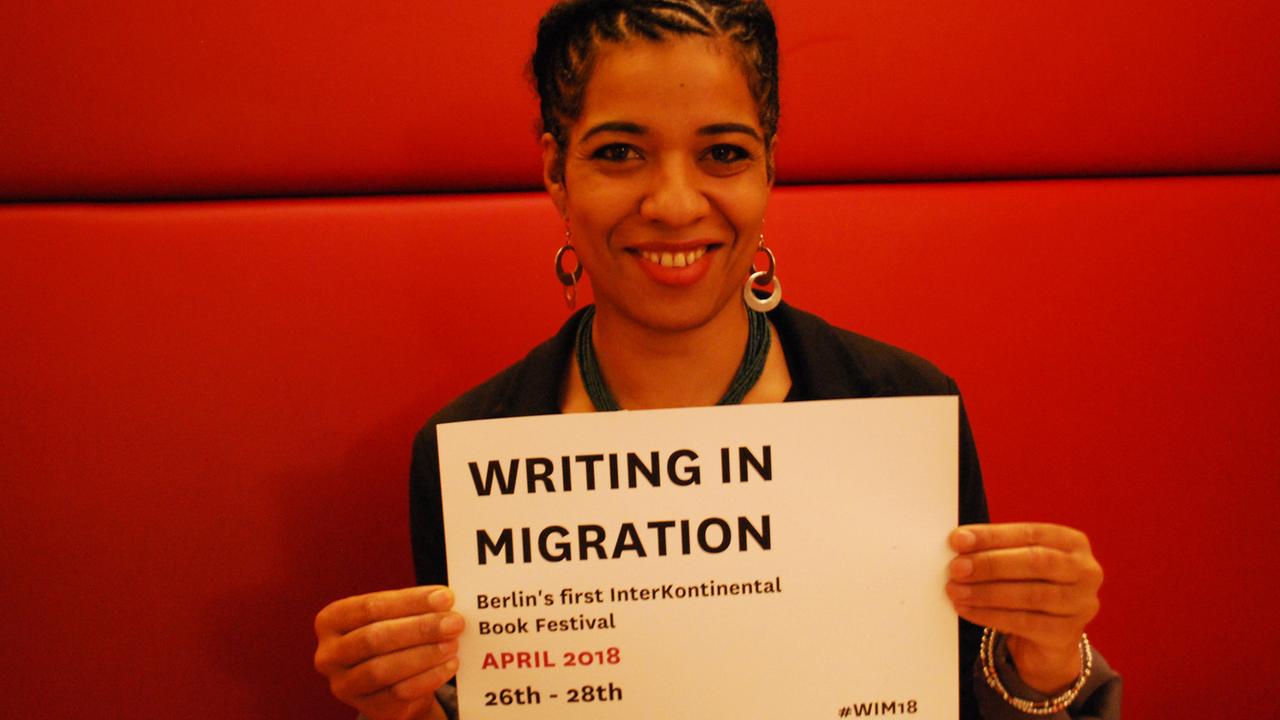 Olumide Popoola, die Kuratorin von "Writing in Migration" hält ein Schild auf dem das Datum des Literaturfestivals zu sehen ist: 26.-28.4.2018