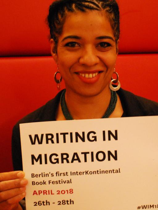 Olumide Popoola, die Kuratorin von "Writing in Migration" hält ein Schild auf dem das Datum des Literaturfestivals zu sehen ist: 26.-28.4.2018