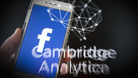 Zu sehen ist ein blaues Facebook Logo auf einem Smartphone, darunter der Schriftzug der Datgenfirma "Cambridge Analytica". 