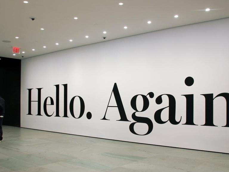 Menschen stehen am schwarzen Schriftzug "Hello Again" von Haim Steinbach im New Yorker Museum of Modern Art.