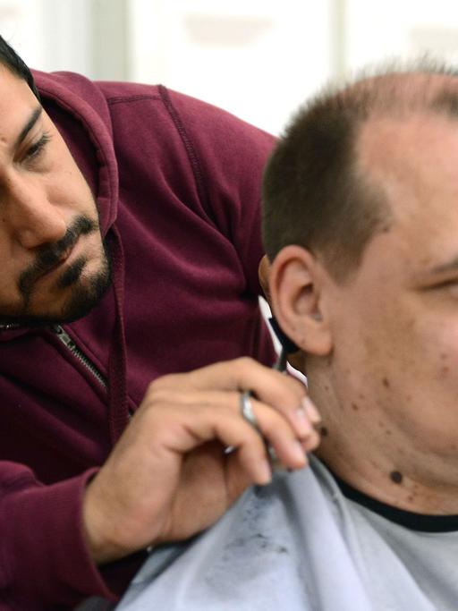 Ein syrischer Flüchtling schneidet einem Deutschen die Haare.