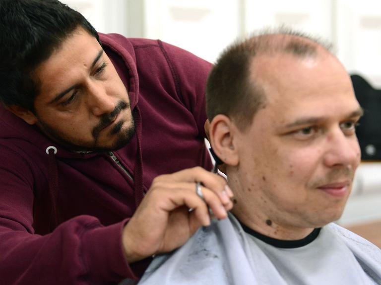 Ein syrischer Flüchtling schneidet einem Deutschen die Haare.