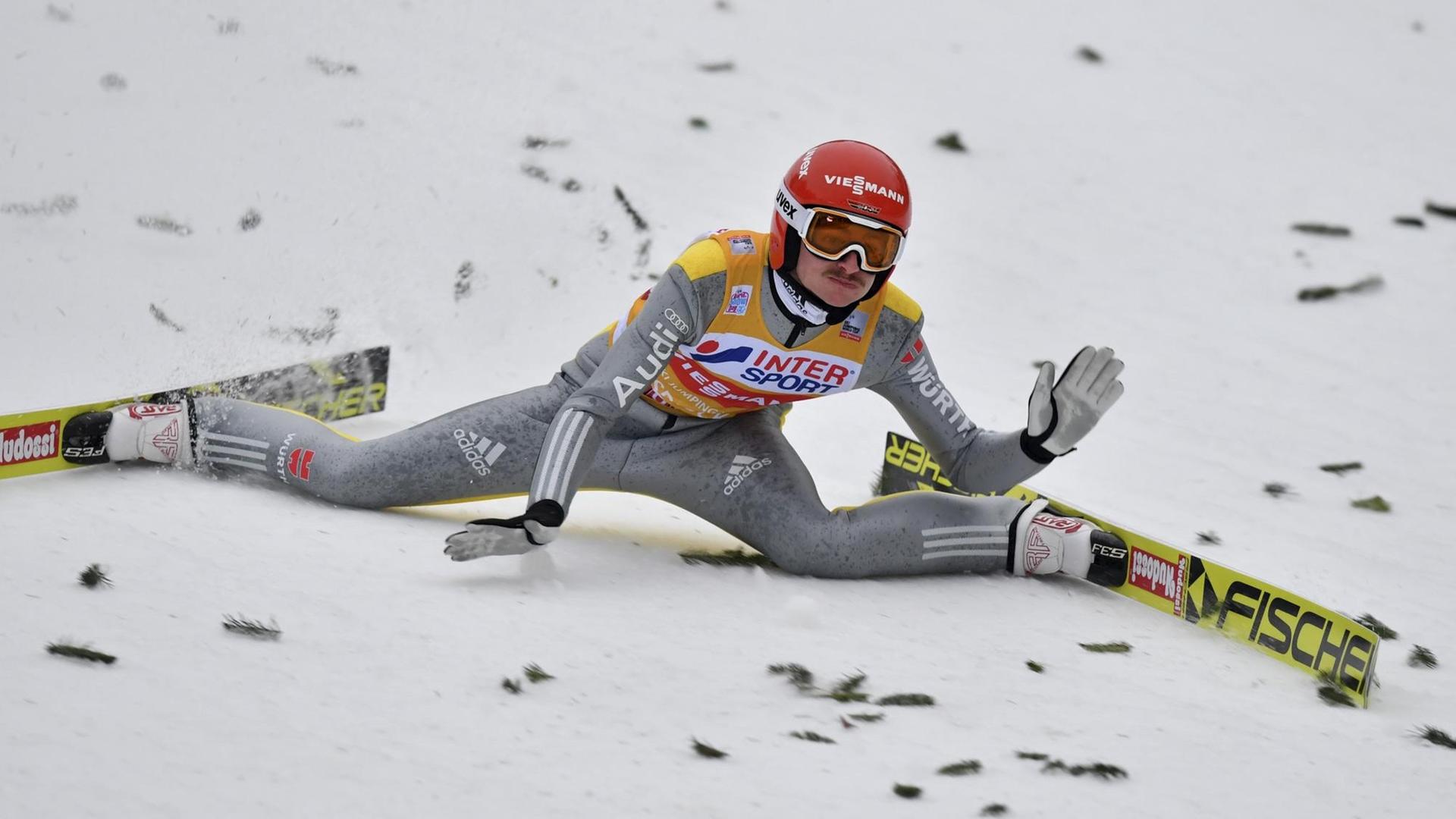 Der Ski-Springer sitzt nach dem Sturz im Schnee.