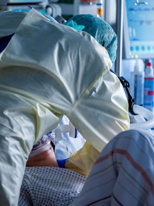 Ein Mitarbeiter richtet bei einer an Covid-19 erkrankten Patientin in einem Zimmer des besonders geschützten Teils der Intensivstation des Universitätsklinikums Greifswald die Beatmungsmaske.