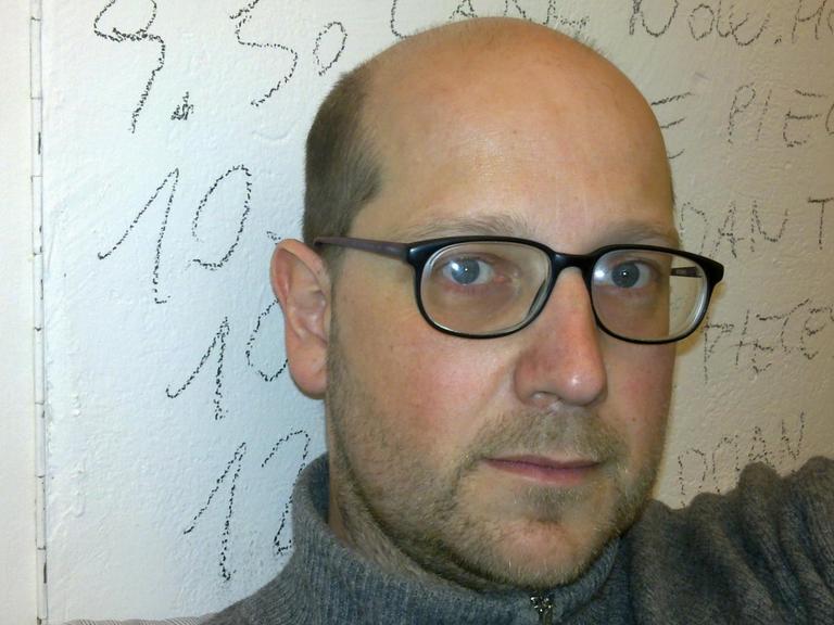 Der steirische Komponist Klaus Lang schaut in die Kamera. Er trägt einen Rollkragenpullover und eine Brille.
