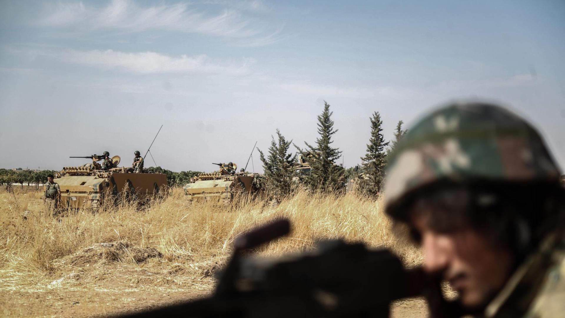 Ein von der Türkei unterstützte Rebell der Syrischen Nationalarmee richtet seine Waffe aus, während im Hintergrund türkische Panzer vorbeifahren